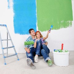 ett ungt par sitter på golvet med en pensel i händerna framför väggen, som är nymålad blå och grön