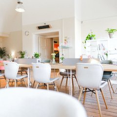 ljus matsal med långbord, vita stolar och inomhusväxter